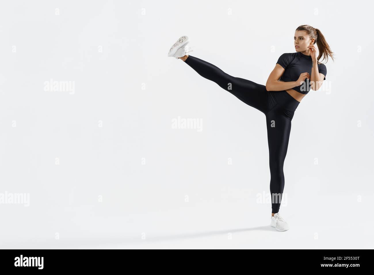 Entraînement sportif assuré pour les femmes, baskets d'entraînement pour les jambes, air de coups de pied dans des vêtements de sport. Femme musclée entraînée donnant un coup de pied avec les pieds relevés, exercice kickboxing Banque D'Images