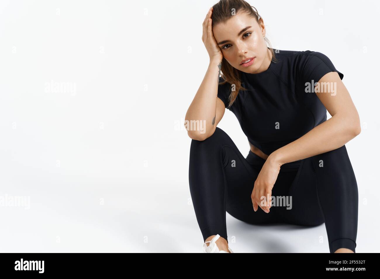 Sport et femmes. Une athlète féminine s'assoit sur le sol après l'entraînement. Posez une femme en bonne santé et formée au repos pendant la séance d'entraînement, regardez l'appareil photo, blanc Banque D'Images