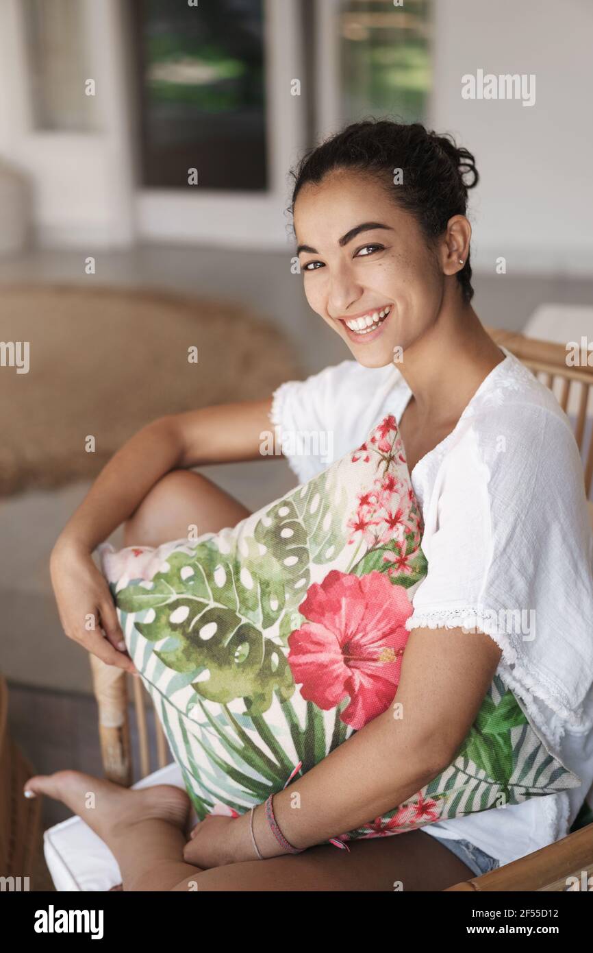 Notion de tendresse, d'émotions et de confort. Tir vertical mignonne hispanique brune femme en t-shirt blanc, jambes assis croisées dans confortable rotin Banque D'Images