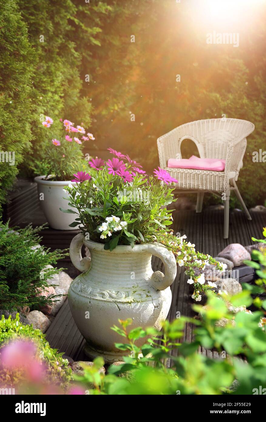 Jardin paisible, ensoleillé et chaleureux, terrasse avec fleurs dans des pots en argile et chaise en osier Banque D'Images