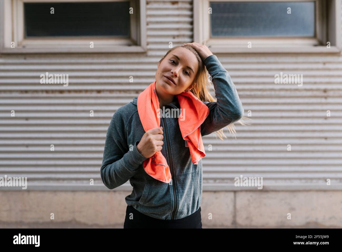 sportswoman souriant avec main dans les cheveux tenant une serviette en position debout contre le mur Banque D'Images