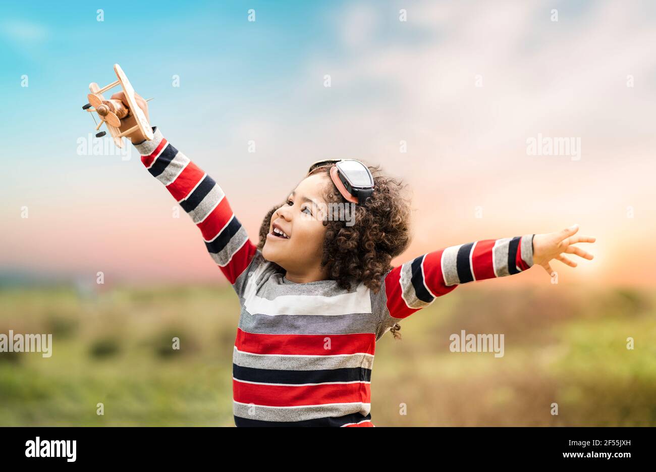 Joyeux garçon mignon jouant avec un jouet en bois avion dans la nature au coucher du soleil Banque D'Images