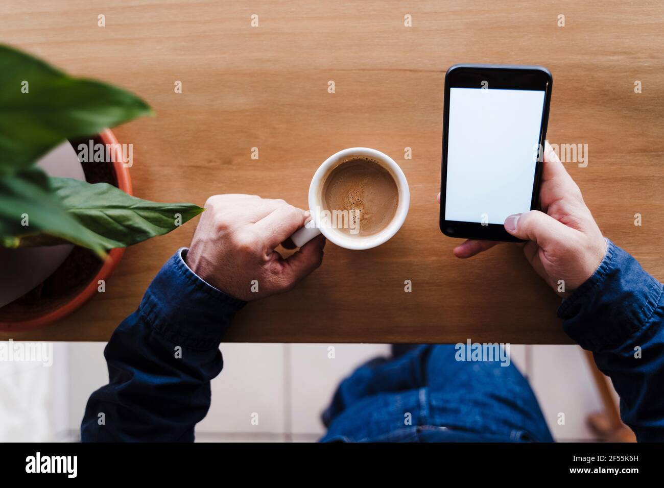 Travailleur indépendant utilisant un téléphone portable tout en tenant une tasse à café au bureau Banque D'Images