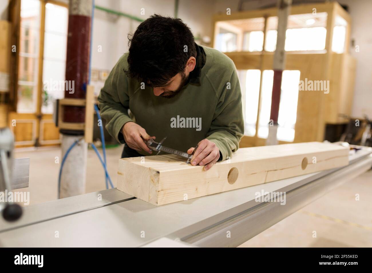 Menuisier mâle mesurant le bois avec pied à coulisse en atelier Banque D'Images