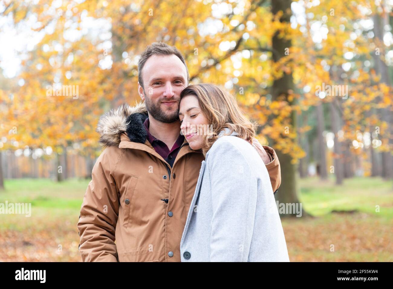 Homme souriant en se tenant debout avec le bras autour de la femme à forêt Banque D'Images
