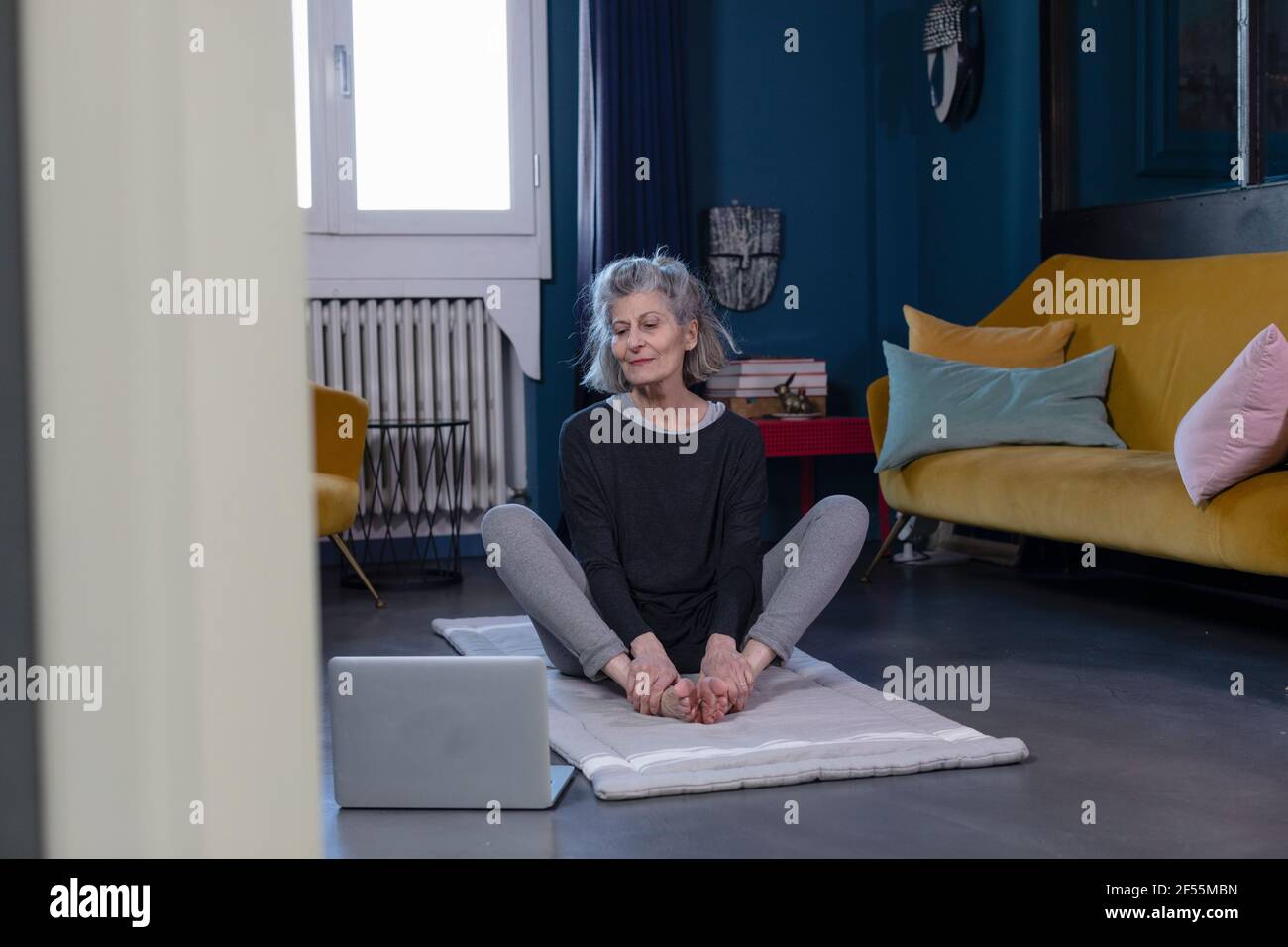 Femme senior faisant du yoga par le biais de tutoriel en ligne sur ordinateur portable à accueil Banque D'Images