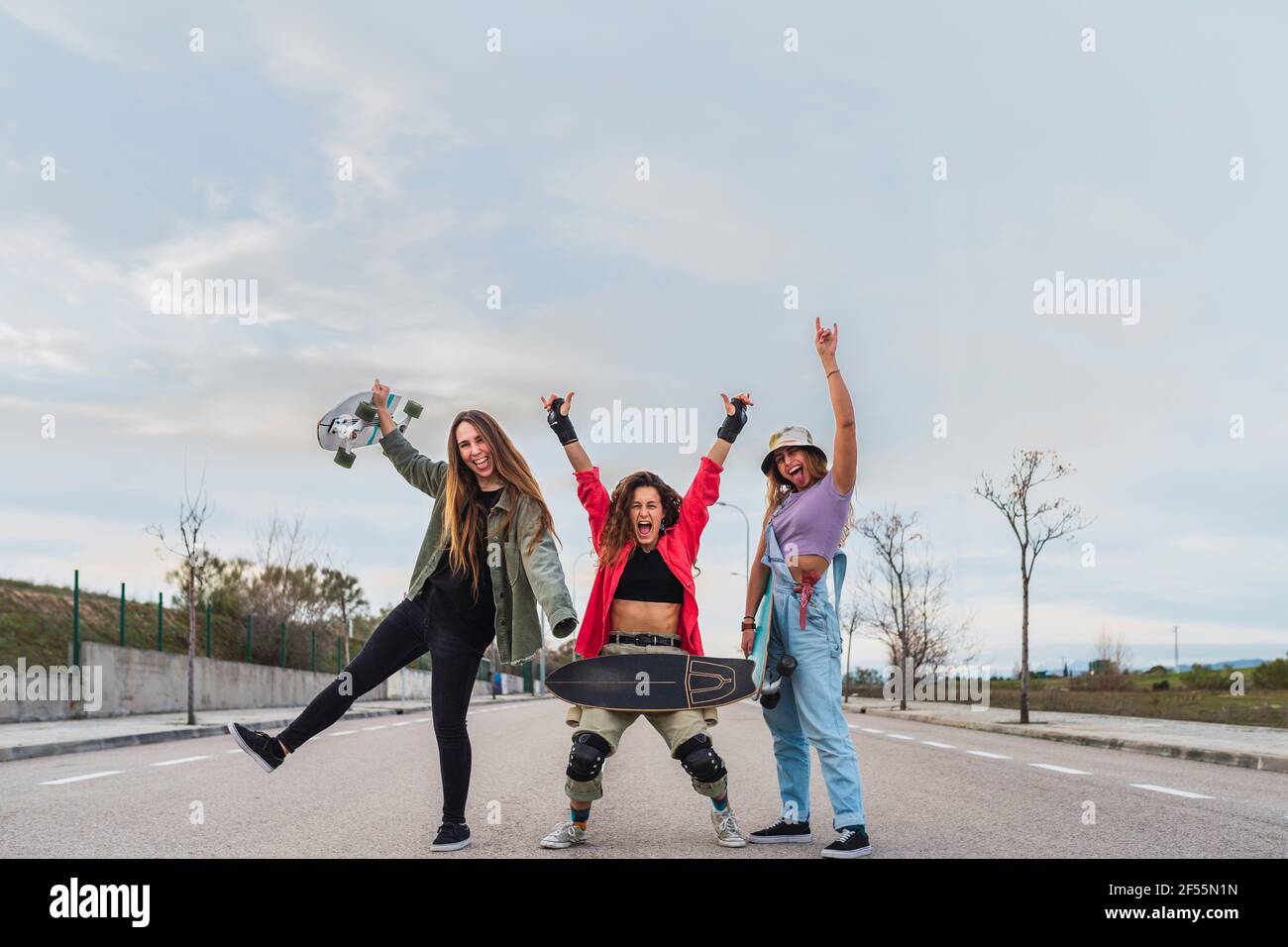 Des amies gaies avec un skateboard qui fait des gestes sur la route Banque D'Images