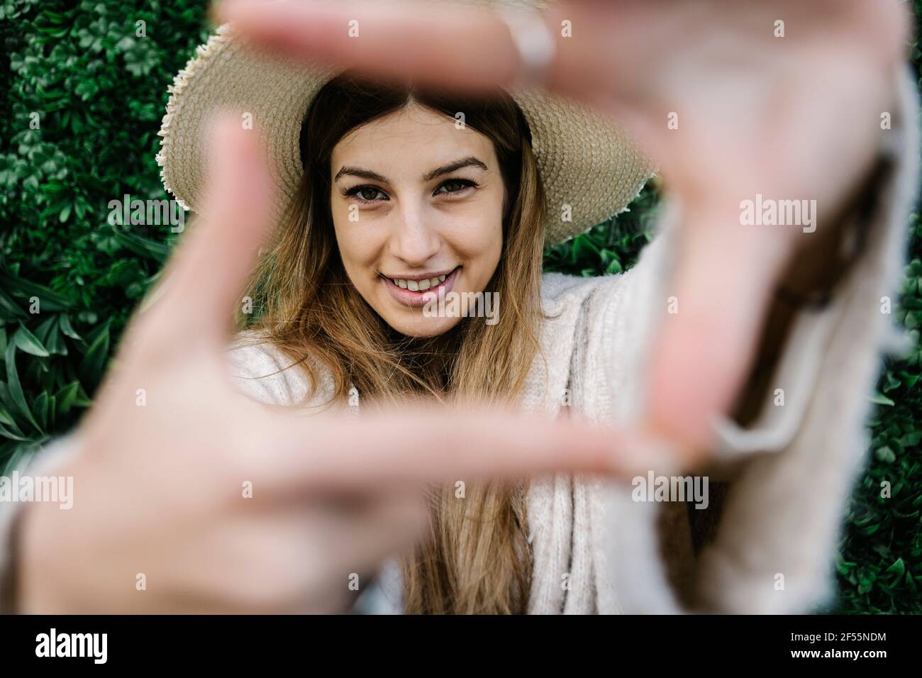 Femme souriante regardant à travers le cadre du doigt Banque D'Images