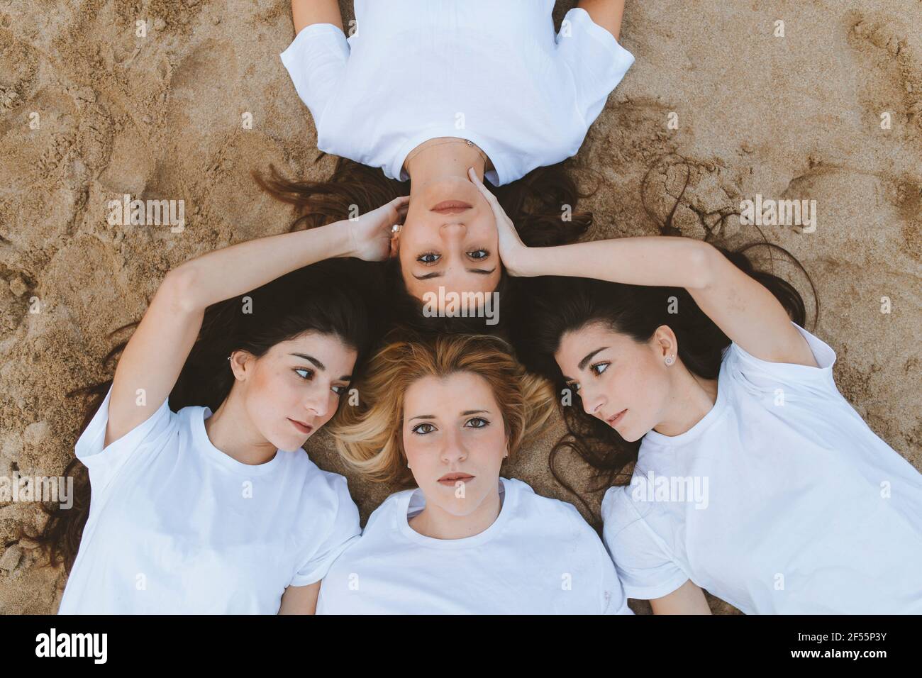 Les jeunes femmes touchent une amie tout en étant allongées sur le sable Banque D'Images