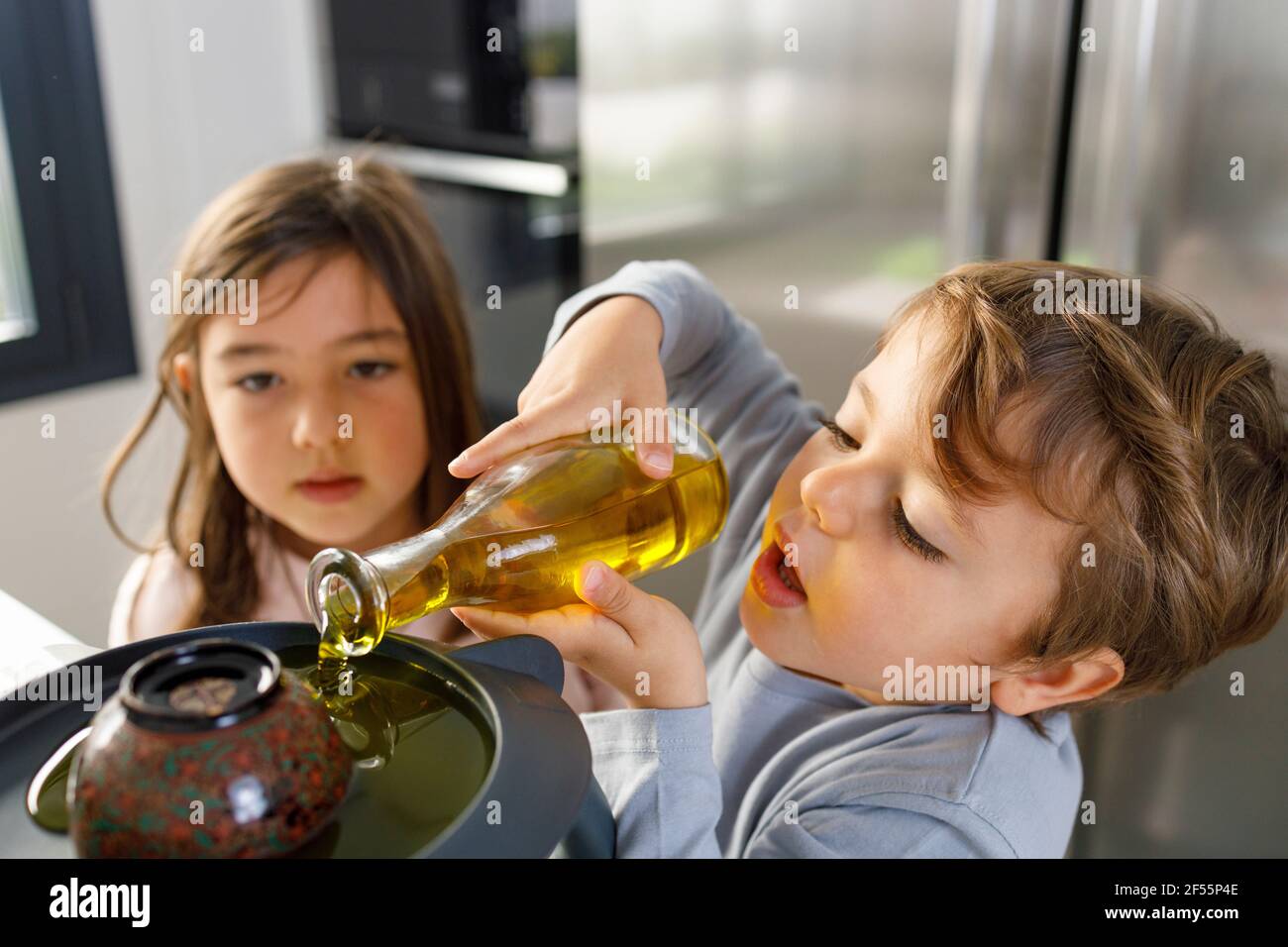 Un adorable garçon souriant verse du jaune d'œuf dans un mixeur de pâte dans la cuisine Banque D'Images