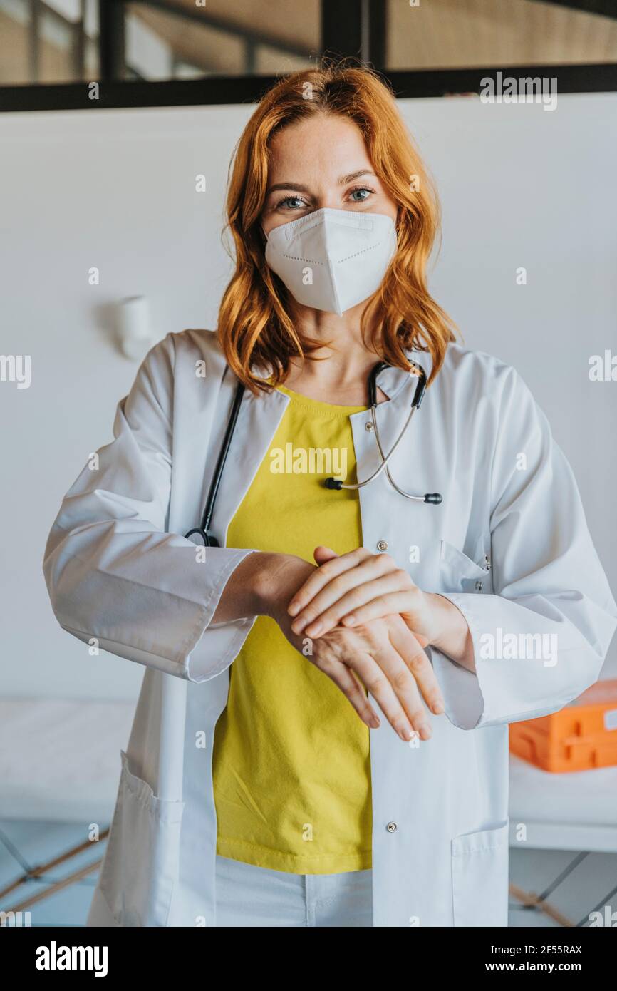 Médecin adulte moyen portant un masque facial de protection se nettoyant les mains avec assainisseur en se tenant à la clinique Banque D'Images