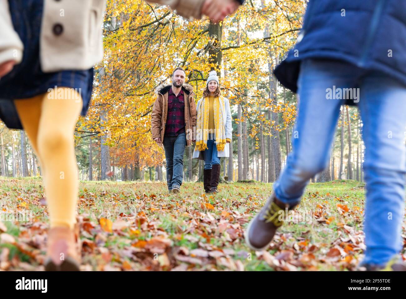 Enfants jouant en courant avec des parents marchant en arrière-plan à forêt Banque D'Images