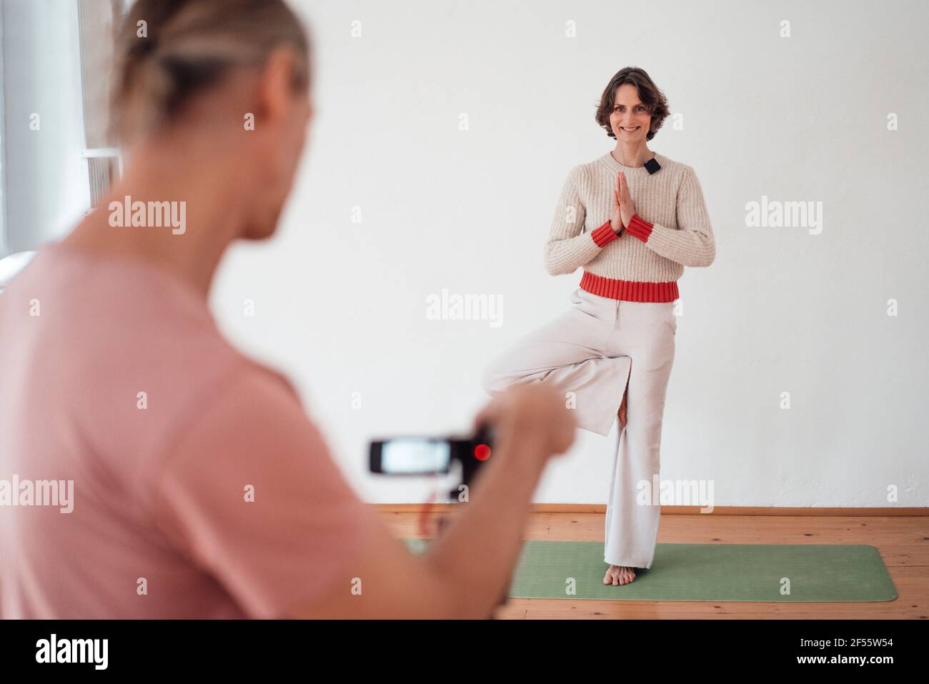 Homme filmant femme instructeur pratiquant l'arbre poser le yoga à la santé studio Banque D'Images