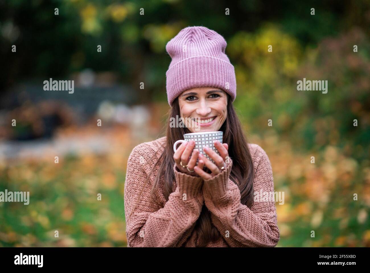 Portrait d'une belle femme portant un chapeau tricoté rose debout à l'extérieur avec tasse dans les mains Banque D'Images