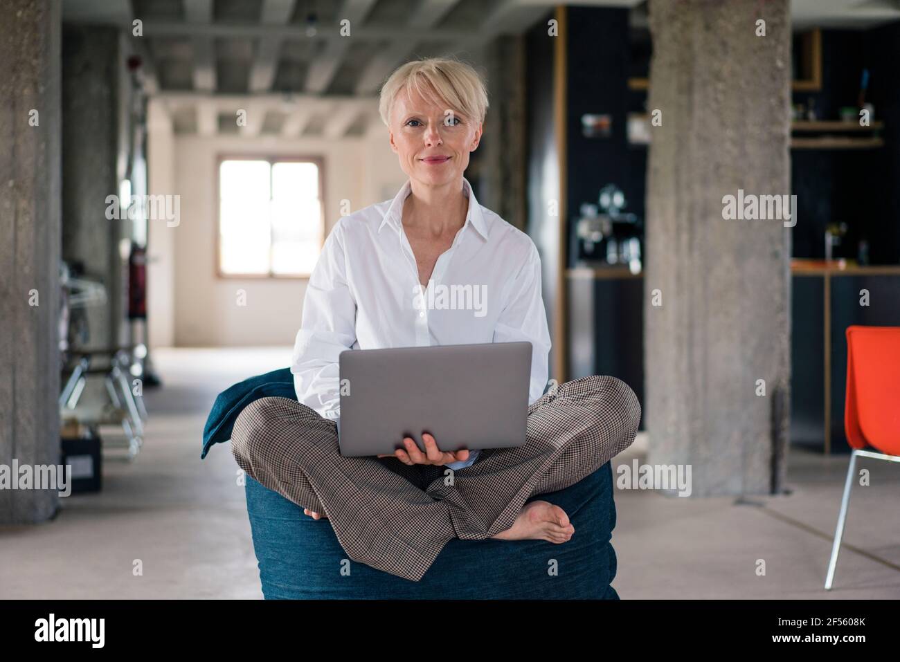 Travailleur indépendant souriant tenant un ordinateur portable assis dans un sac à bandoulière accueil Banque D'Images