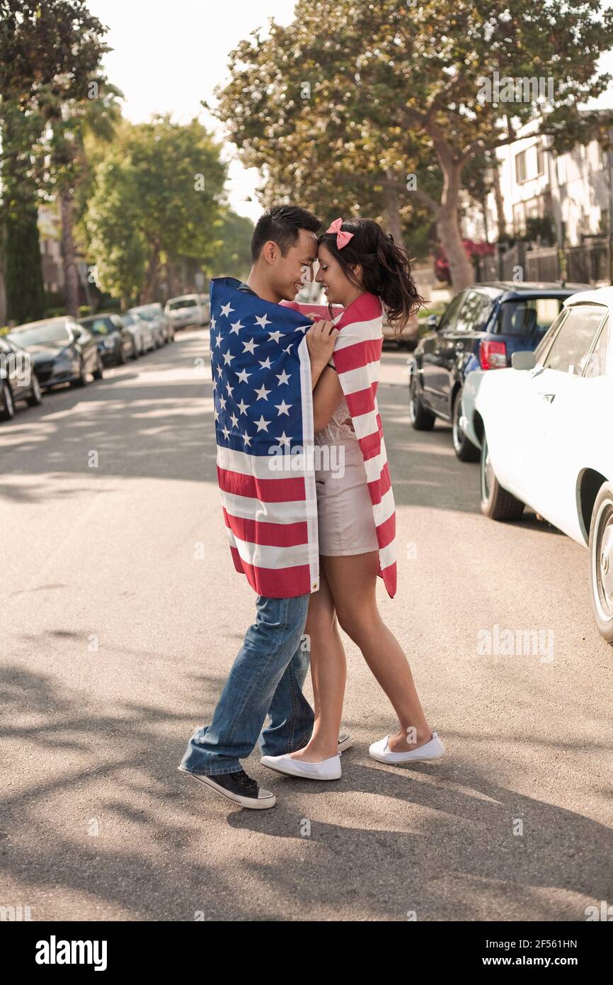 Petite amie et petit ami enveloppés dans un drapeau américain debout face à face à la rue dans la ville Banque D'Images