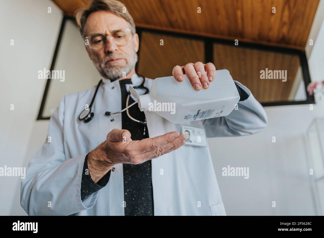 Médecin mature utilisant un désinfectant pour les mains en se tenant à la clinique Banque D'Images