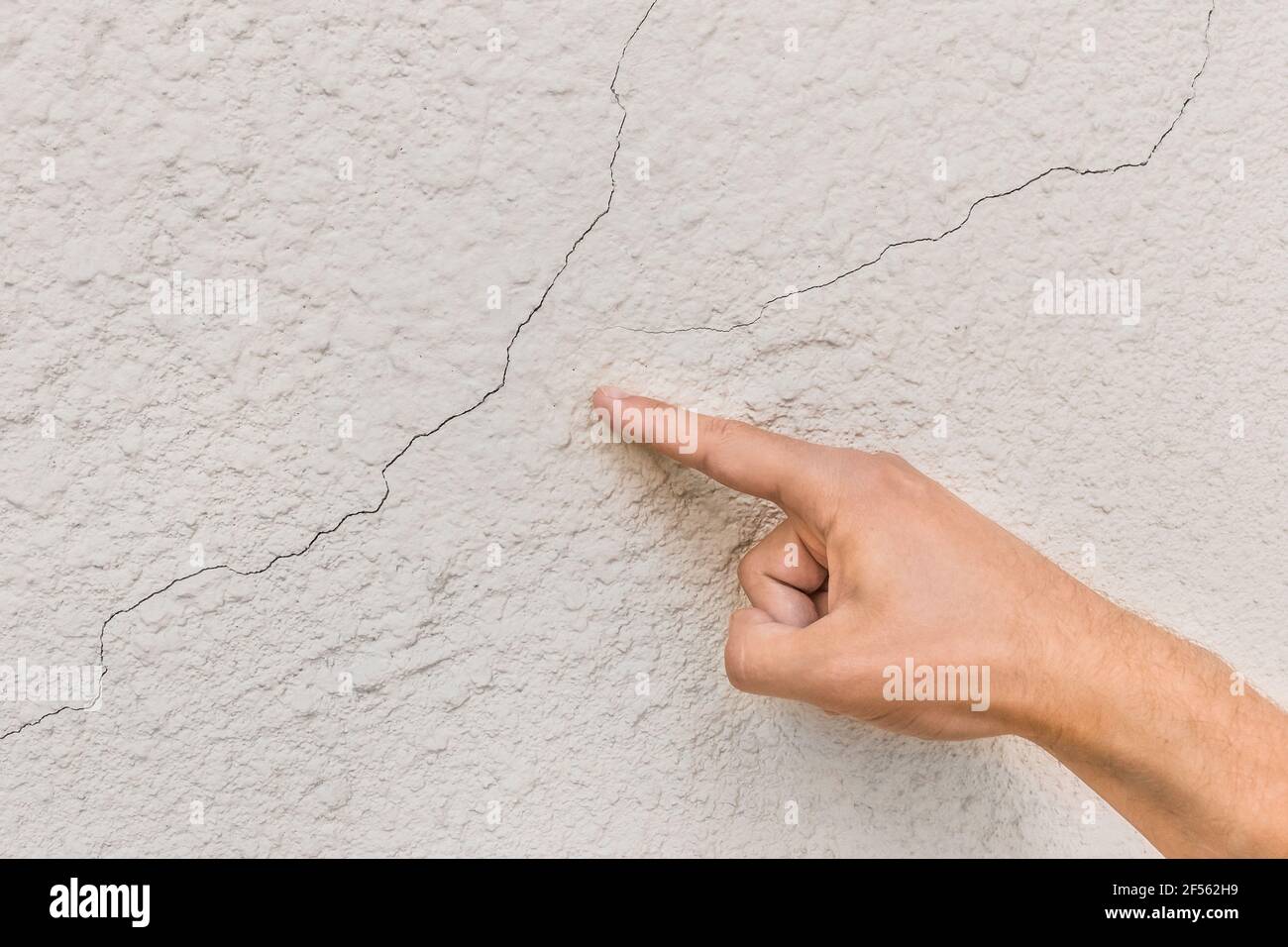La main d'un ouvrier de construction de sexe masculin pointe des fissures sur un fond de mur cassé blanc. Concept de rénovation ou de réparation. Banque D'Images