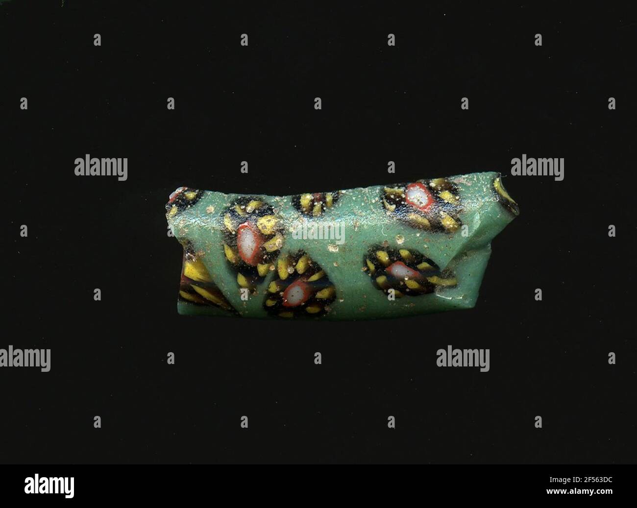 Fragment d'un vaisseau. Une faible courbure du fragment de verre permet l'affectation à un vaisseau, éventuellement le bord d'une coque. Le verre turquoise montre plusieurs fleurs dans la technologie millefiori. Ils se composent d'un point blanc avec un contour rouge pour tracer des points jaunes avec un contour noir comme pétales. Pour la production, des verres de différentes couleurs ont été formés en tubes et en tiges. Elles étaient comprimées et chauffées, ce qui entraînait une longue barre. Le verre coupé en tranches de ​​now avait des motifs amorphes ou floraux différents. Par la suite, plusieurs de ces plaquettes ont été repliées ensemble, réchauffées à nouveau et pressées en forme vasculaire. Banque D'Images