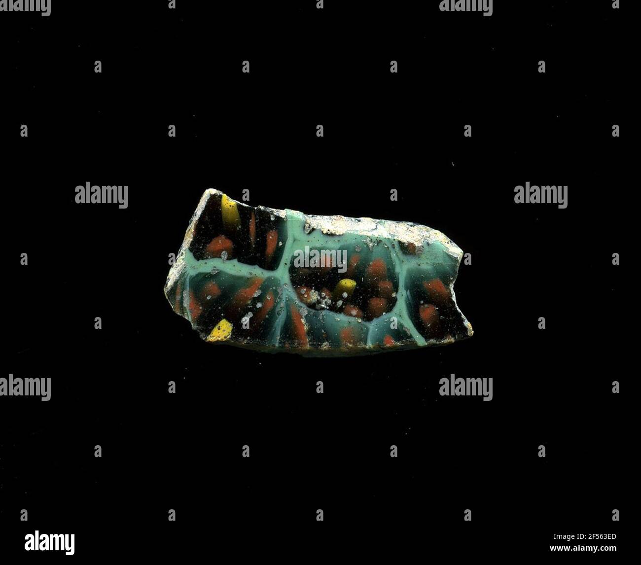 Fragment d'un vaisseau. Une faible courbure du fragment de verre permet l'affectation à un vaisseau, éventuellement à une coque. Le shard vert menthe montre plusieurs fleurs dans la technologie millefiori. Un cercle jaune est entouré de plusieurs cercles rouges avec un contour noir. Les représentations sont légèrement déformées. Pour la production, des verres de différentes couleurs ont été formés en tubes et en tiges. Elles étaient comprimées et chauffées, ce qui entraînait une longue barre. Le verre coupé en tranches de ​​now avait des motifs amorphes ou floraux différents. Par la suite, plusieurs de ces plaquettes ont été pliées, chauffées à nouveau et pressées en forme vasculaire. Burr Banque D'Images