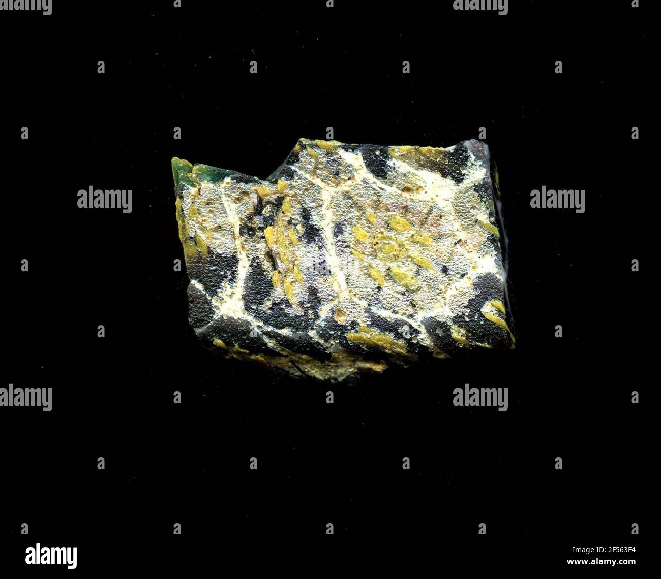 Fragment d'un vaisseau. Une faible courbure du fragment de verre permet l'affectation à un vaisseau, éventuellement à une coque. Le sol violet est traversé par une grille de lignes blanches rappelant les nids d'abeilles. Dans les champs, on peut voir des fleurs dans la technologie millefiori. Pour obtenir un point jaune d'autres points jaunes comme pétales. Une autre fleur peut être vue au bord de la fracture : un demi-cercle avec des lignes jaunes et bleues. Pour la production, des verres de différentes couleurs ont été façonnés sur des tubes et des poteaux. Elles étaient comprimées et chauffées, ce qui entraînait une longue barre. Le verre coupé en tranches de ​​now avait des motifs amorphes ou floraux différents Banque D'Images