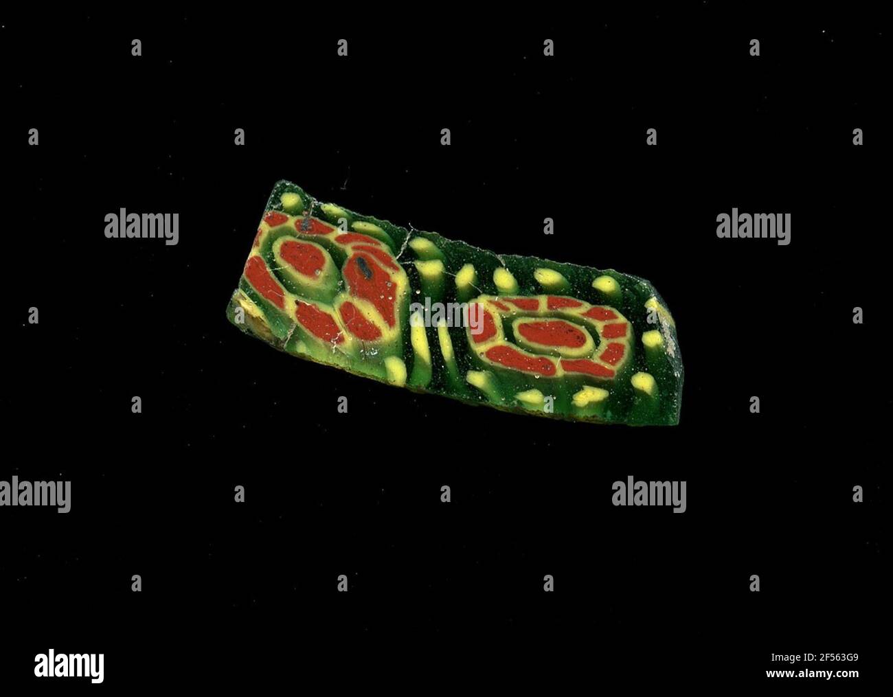 Fragment d'un vaisseau. Une faible courbure du fragment de verre permet l'affectation à un vaisseau, éventuellement à une coque. Le shard vert montre deux fleurs dans la technologie millefiori. Un point rouge avec un contour jaune mène à une bande de points rouges avec un contour jaune. C'est pourquoi des points circulaires jaunes sont visibles. Pour la production, des verres de différentes couleurs ont été formés en tubes et en tiges. Elles étaient comprimées et chauffées, ce qui entraînait une longue barre. Le verre coupé en tranches de ​​now avait des motifs amorphes ou floraux différents. Par la suite, plusieurs de ces plaquettes ont été repliées ensemble, réchauffées à nouveau et pressées dans le système vasculaire Banque D'Images