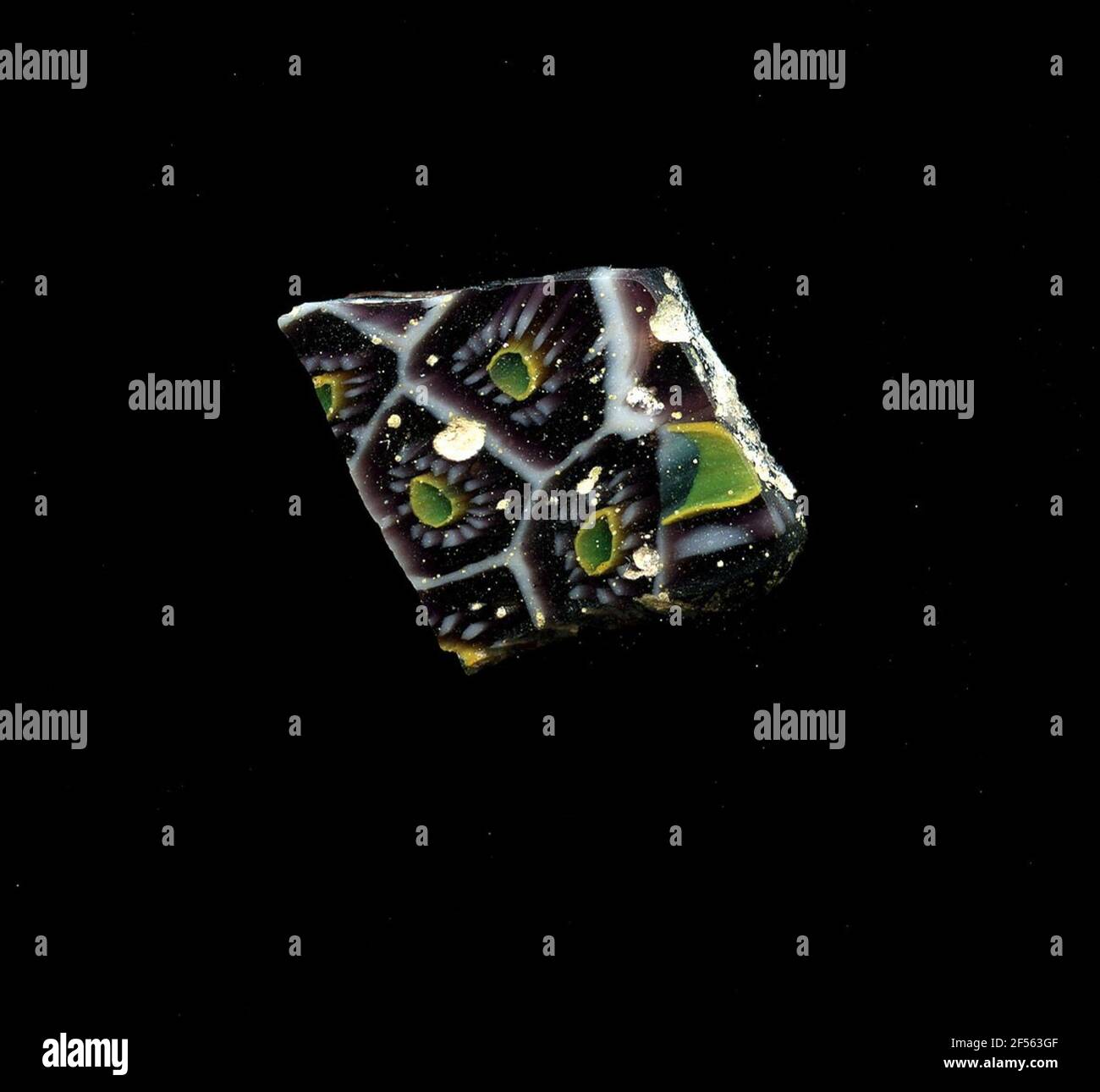 Fragment d'un vaisseau. Une faible courbure du fragment de verre permet l'affectation à un vaisseau, éventuellement à une coque. Le shard violet est croisé avec une grille de lignes blanches qui rappellent les nids d'abeilles. Au centre, il y a un point bleu avec un contour jaune pour regrouper les points blancs circulaires sous forme de pétales. Pour la production, des verres de différentes couleurs ont été formés en tubes et en tiges. Elles étaient comprimées et chauffées, ce qui entraînait une longue barre. Le verre coupé en tranches de ​​now avait des motifs amorphes ou floraux différents. Par la suite, plusieurs de ces plaquettes ont été repliées ensemble, réchauffées à nouveau et pressées dans la vascul Banque D'Images