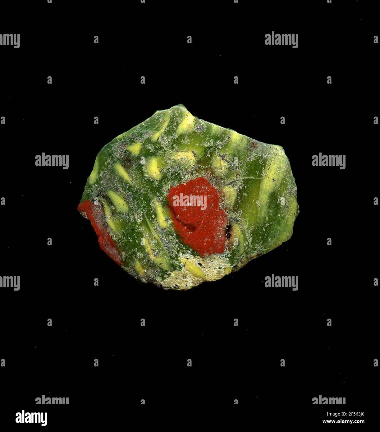 Fragment d'un vaisseau. Une faible courbure du fragment de verre permet l'affectation à un vaisseau. Dans le verre vert, on peut voir des points jaunes fins dans la technologie millefiori. Les fleurs se composent d'un noyau angulaire rouge pour se trouver les petits points jaunes circulaires sous forme de pétales. Pour la production, des verres de différentes couleurs ont été moulés dans des tubes et des tiges. Elles étaient comprimées et chauffées, ce qui entraînait une longue barre. Le verre coupé en tranches de ​​now avait des motifs amorphes ou floraux différents. Par la suite, plusieurs de ces plaquettes ont été repliées ensemble, réchauffées à nouveau et pressées en forme vasculaire. Burry pour l'élaboration Banque D'Images