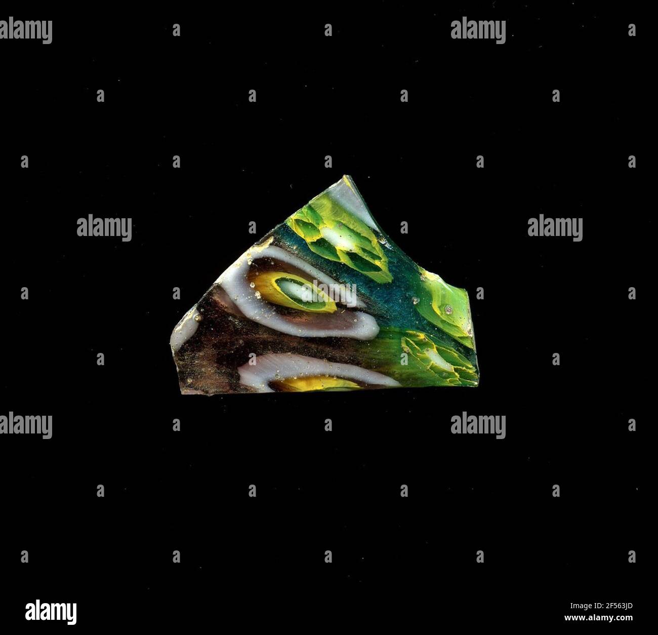 Fragment d'un vaisseau. Une faible courbure du fragment de verre permet l'affectation à un vaisseau, éventuellement à une coque. Dans le verre violet et bleu, deux formes de fleurs peuvent être vues dans la technologie millefiori. Sur une raison violette, vous pouvez voir des fleurs composées d'anneaux concentriques dans la séquence de couleurs blanc, bleu, jaune, violet et blanc. Sur un fond bleu, se trouve autour d'un milieu blanc jaune bordé de pétales bleu trapézoïdal. Pour la production, des verres de différentes couleurs ont été façonnés sur des tubes et des tiges. Elles étaient comprimées et chauffées, ce qui entraînait une longue barre. Le verre coupé en tranches de ​​now avait un o amorphe différent Banque D'Images