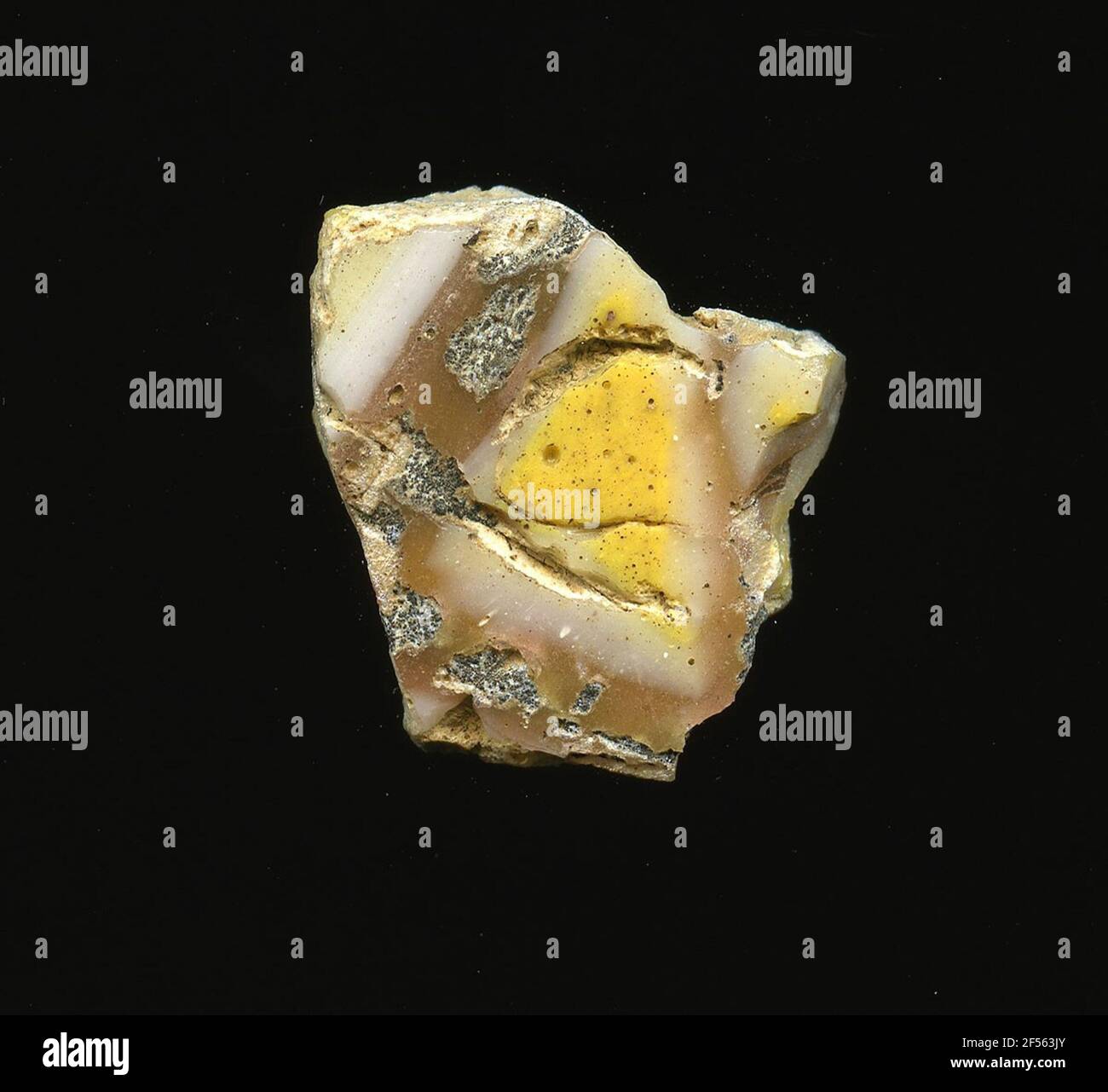 Fragment d'un vaisseau. Une faible courbure du fragment de verre permet l'affectation à un vaisseau, éventuellement à une coque. Le fragment montre sur la raison marron clair un motif géométrique. Autour des triangles jaunes est une bande de verre blanc à reconnaître, à laquelle des triangles similaires se connectent. Sur la surface, des traces de corrosion ou de sintres peuvent être observées. Pour la production, des verres de différentes couleurs ont été formés en tubes et en tiges. Elles étaient comprimées et chauffées, ce qui entraînait une longue barre. Le verre coupé en tranches de ​​now avait des motifs amorphes ou floraux différents. Par la suite, plusieurs de ces plaquettes ont été repliées ensemble, AG chauffé Banque D'Images