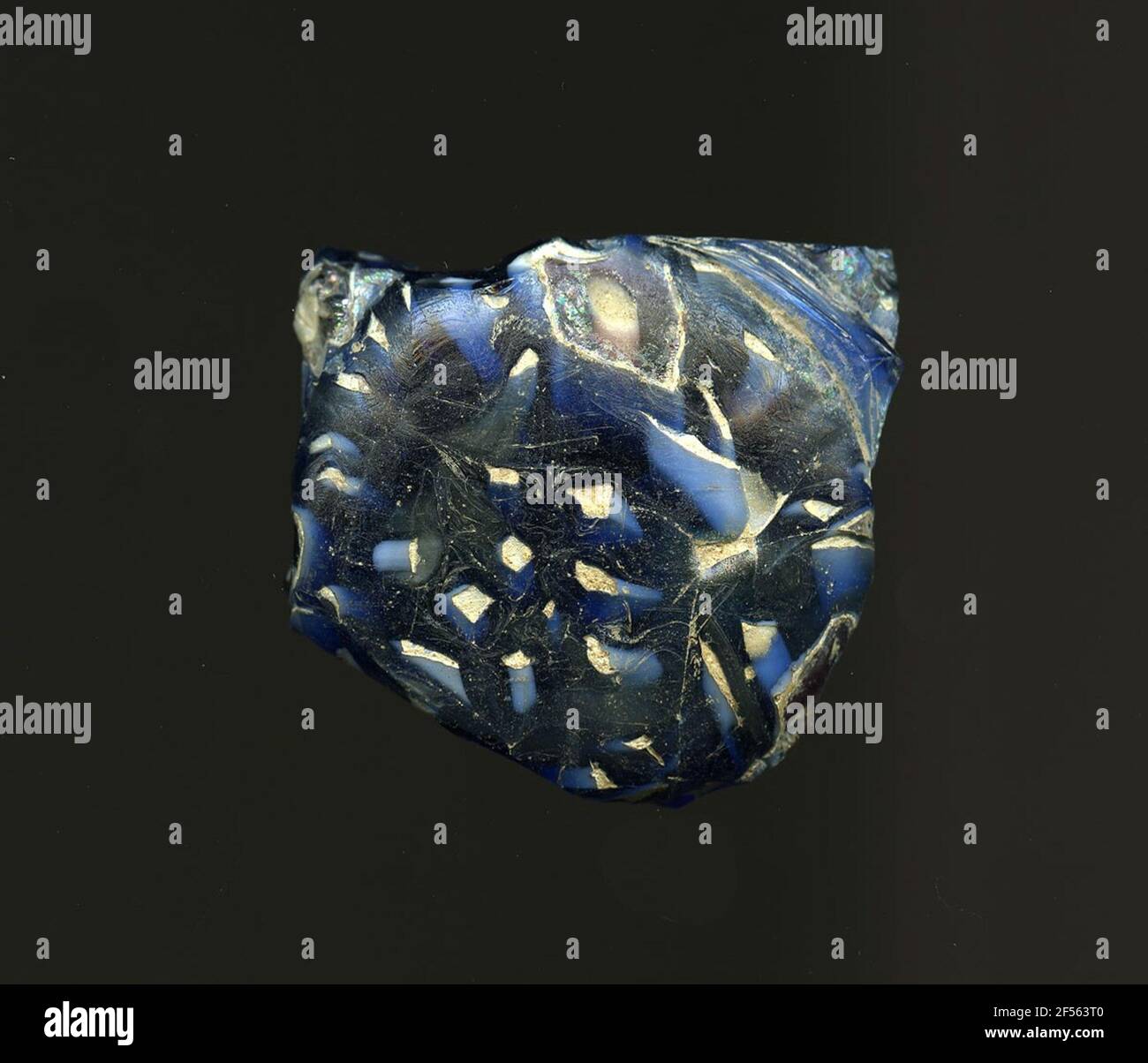 Fragment d'un vaisseau. Une faible courbure du fragment de verre permet l'affectation à un vaisseau, éventuellement à une coquille ou à une bouteille. Le verre bleu foncé à travers différentes formes géométriques blanches comme les petits carrés, les points d'édouété ou les cercles. Sur ces formulaires, le verre est bleu clair. Pour la production, des verres de différentes couleurs ont été façonnés sur des tubes et des tiges. Elles étaient comprimées et chauffées, ce qui entraînait une longue barre. Le verre coupé en tranches de ​​now avait des motifs amorphes ou floraux différents. Par la suite, plusieurs de ces plaquettes ont été repliées ensemble, réchauffées à nouveau et pressées en forme vasculaire. Burry pour l'élaboration Banque D'Images