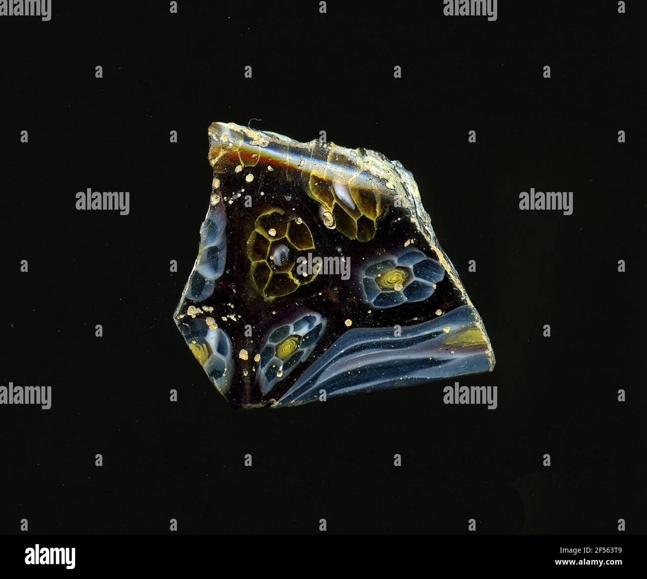 Fragment d'un vaisseau. Une faible courbure du fragment de verre permet l'affectation à un vaisseau, éventuellement à une coque. En verre violet, deux formes de fleurs sont présentées dans la technologie millefiori. L'un consiste en un point blanc au milieu pour entourer les contours jaunes des pétales proches, les autres d'une spirale étroite en tant que noyau et les points bleus blancs en tant que pétales. Sur une bordure sont déformées bandes de couleur bleue à blanche. Pour la production, des verres de différentes couleurs ont été formés en tubes et en tiges. Elles étaient comprimées et chauffées, ce qui entraînait une longue barre. Le verre coupé en tranches de ​​now avait de la diffuse Banque D'Images