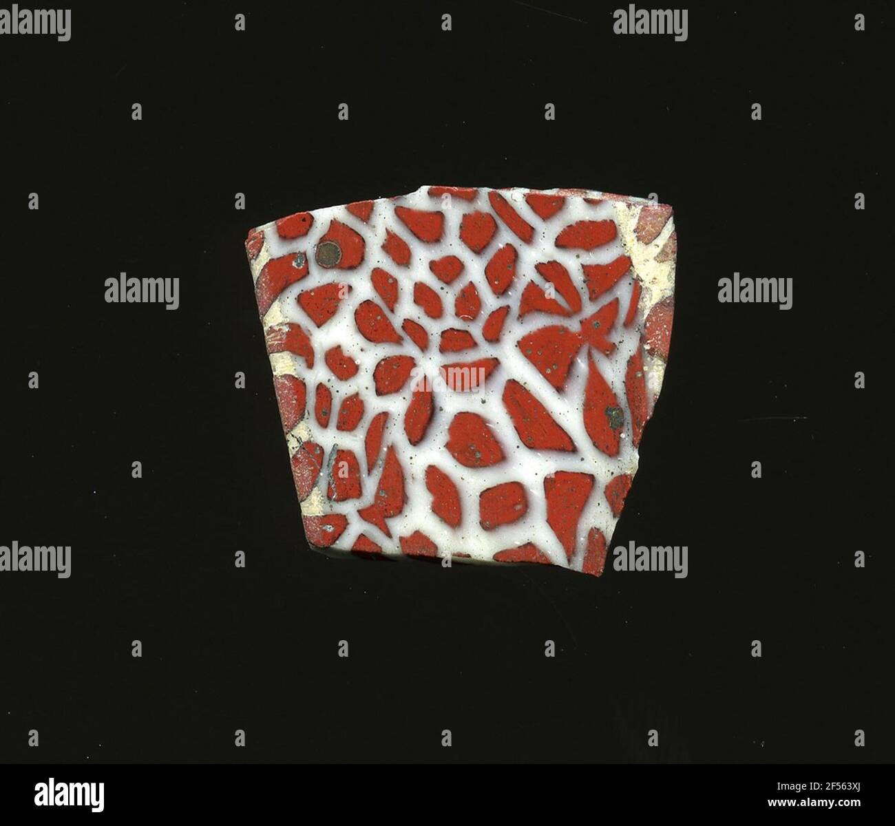 Fragment d'un vaisseau. La faible courbure permet l'affectation de ce fragment à un pot en verre. Sur fond blanc, des taches rouges - en partie avec une fine bordure noire - sont incorporées. La construction du processus de fabrication élaboré et de sa fragilité comprenait le verre aux articles de luxe de l'antiquité. Banque D'Images