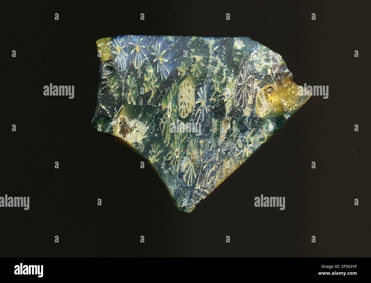 Fragment d'un vaisseau. Une faible courbure du fragment de verre permet l'affectation à un vaisseau. La couleur du verre s'oppose au vert, au bleu et au jaune. On y montre deux types de fleurs dans la technologie millefiori: Un type a un point jaune avec des lignes blanches en forme de faisceau, l'autre un centre blanc et des lignes blanches. Pour la production, des verres de différentes couleurs ont été formés en tubes et en tiges. Elles étaient comprimées et chauffées, ce qui entraînait une longue barre. Le verre coupé en tranches de ​​now avait des motifs amorphes ou floraux différents. Par la suite, plusieurs de ces plaquettes ont été pliées ensemble, réchauffées à nouveau et pr Banque D'Images
