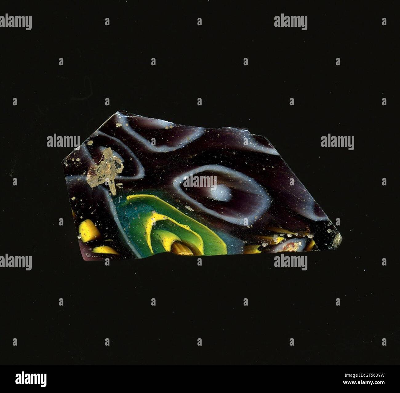 Fragment d'un vaisseau. Une faible courbure du fragment de verre permet l'affectation à un vaisseau, éventuellement à une coque. Le Curbe montre une raison violette plusieurs types de fleurs dans la technique de Millefiori: Un type consiste en un point blanc sur lequel un autre cercle blanc est battu, qui marque les pétales, l'autre est marqué par une ligne en spirale jaune qui est marquée dans l'un finit probablement le point blanc et dont l'espace est bleu apparaît. Au niveau des bords de la cassure, de petits points jaunes sont visibles, qui appartient probablement comme pétales aux autres fleurs. Pour la production, des verres de différentes couleurs ont été façonnés sur des tubes et des tiges. TH Banque D'Images