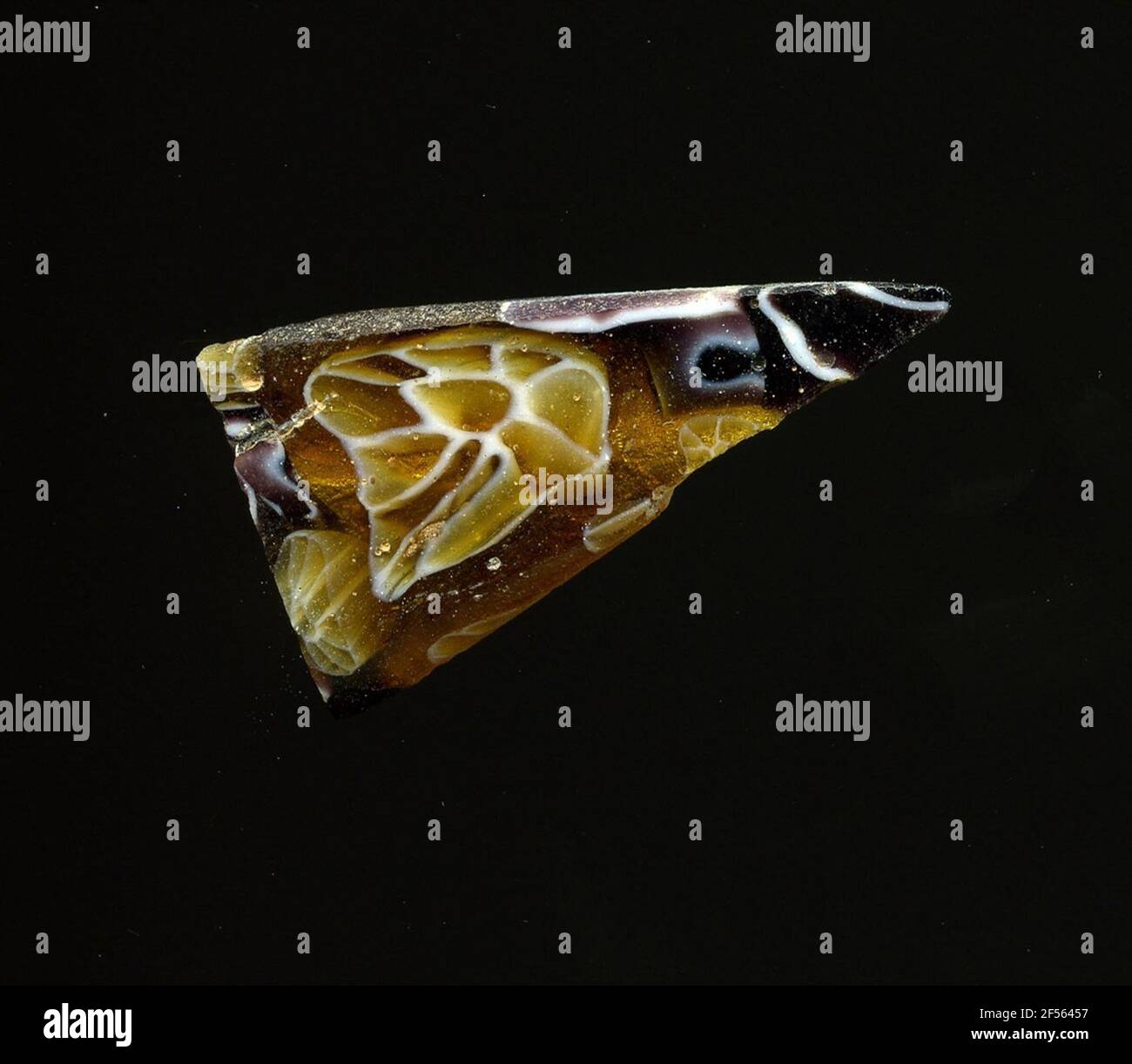 Fragment d'un vaisseau. Une faible courbure du fragment de verre permet l'affectation à un vaisseau, éventuellement à une coque. La couleur du verre passe du brun doré au violet. Sur elle sont des fleurs dans la technologie millefiori pour voir dont les contours (coeur intérieur et pétales) sont entourés de blanc. Les lignes du verre violet sont déformées. Pour la production, des verres de différentes couleurs ont été formés en tubes et en tiges. Elles étaient comprimées et chauffées, ce qui entraînait une longue barre. Le verre coupé en tranches de ​​now avait des motifs amorphes ou floraux différents. Par la suite, plusieurs de ces plaquettes ont été pliées, chauffées à nouveau et presse Banque D'Images