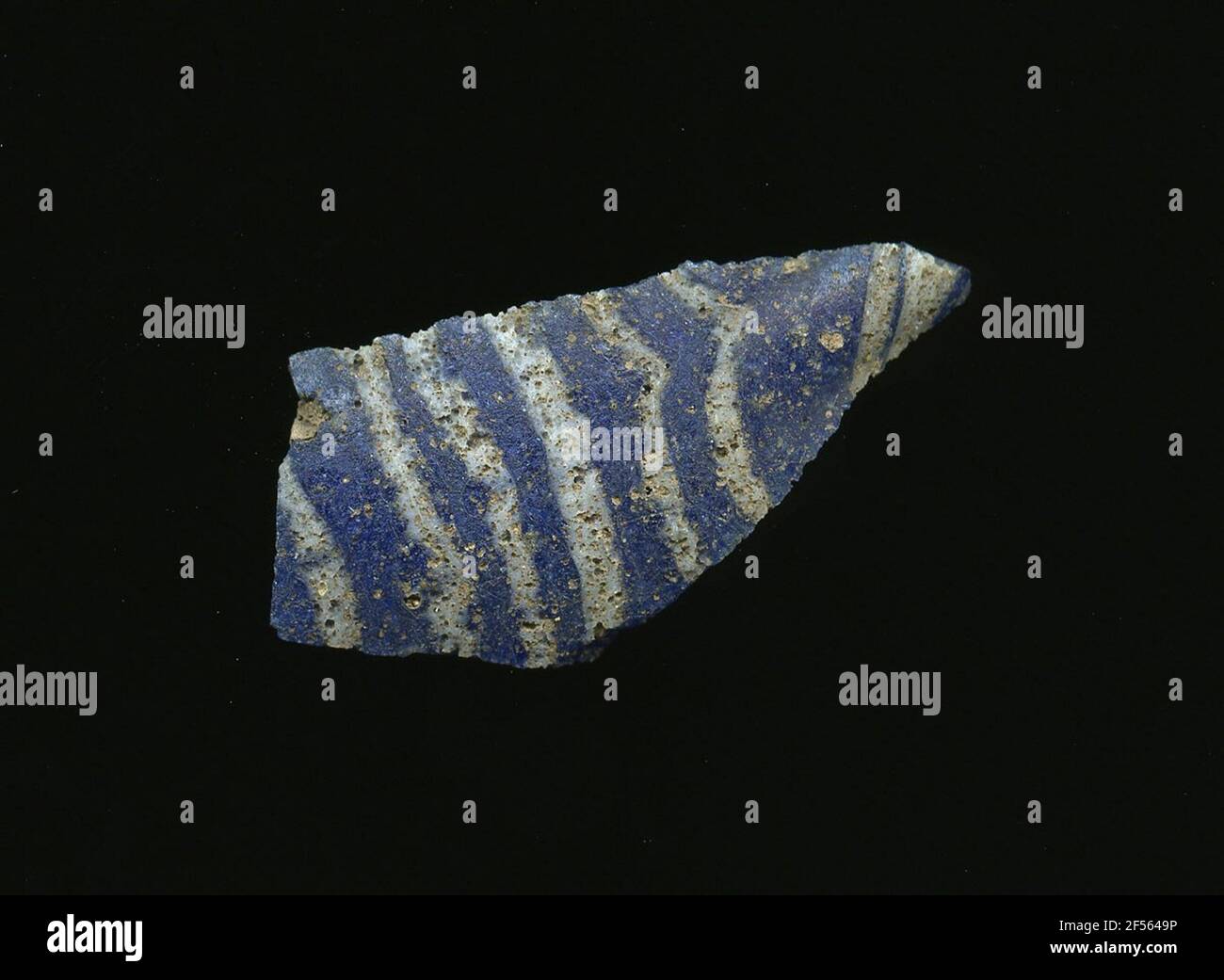 Fragment d'un vaisseau. Une faible courbure du fragment de verre permet l'affectation à un vaisseau, éventuellement à une coque. À travers la vitre bleue, des lignes blanches parallèles tirent. Deux petits points blancs sont visibles à l'arrière. Pour la production différentes verres de couleur aux tubes et tiges ont été formés. En raison du processus de fabrication élaboré et de sa fragilité, le verre a compté aux articles de luxe de l'antiquité. Banque D'Images