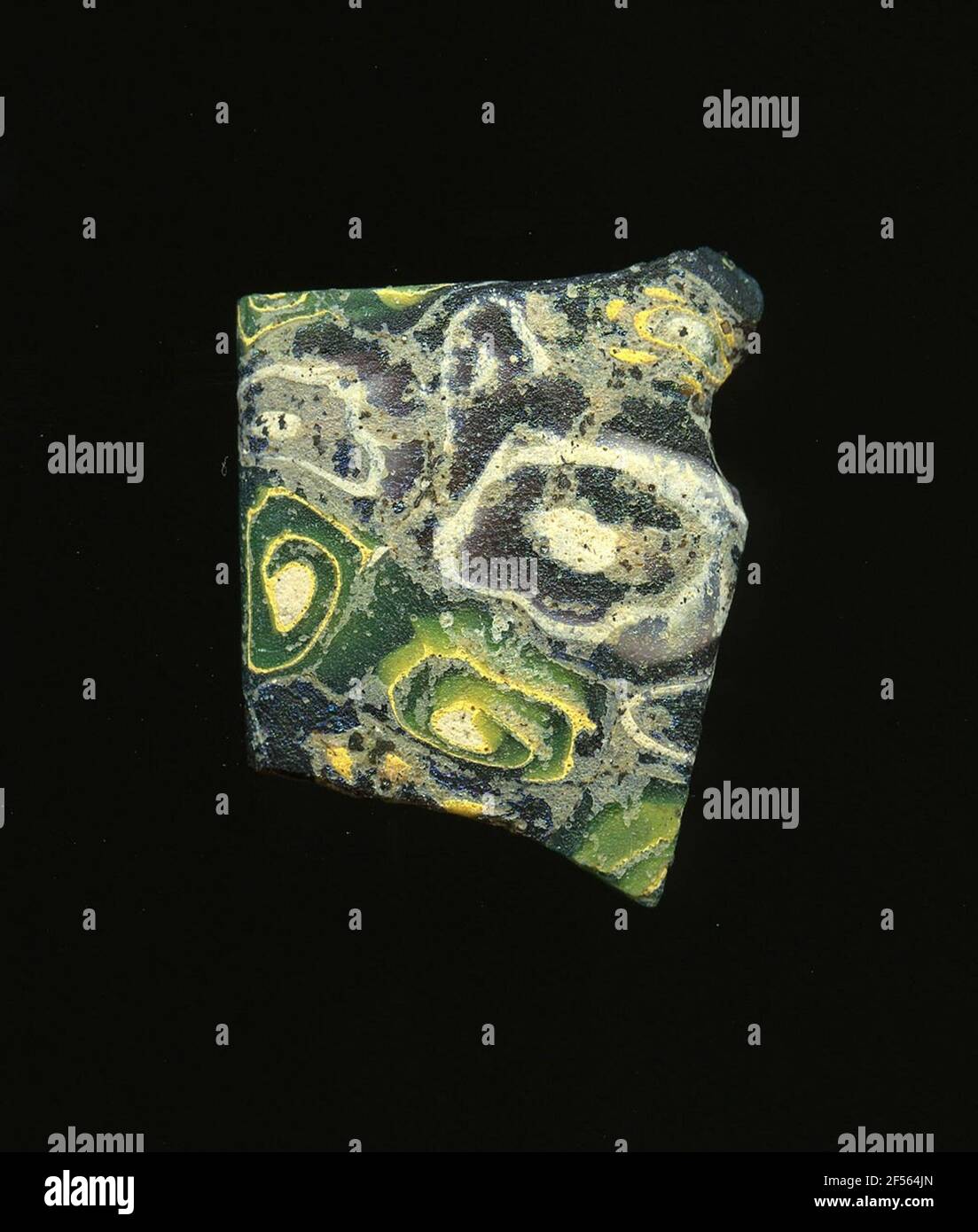 Fragment d'un vaisseau. Une faible courbure du fragment de verre permet l'affectation à un vaisseau. Le shard a des jeux violés vert et foncé sur lesquels les spirales jaune et blanc de différentes tailles peuvent être vues. Pour la production, des verres de différentes couleurs ont été façonnés sur des tubes et des tiges. Elles étaient comprimées et chauffées, ce qui entraînait une longue barre. Le verre coupé en tranches de ​​now avait des motifs amorphes ou floraux différents. Par la suite, plusieurs de ces plaquettes ont été fusionnées, réchauffées à nouveau et formées. Burry pour le processus de fabrication élaboré et sa fragilité comprenait le verre des articles de luxe de l'antiquité. Banque D'Images