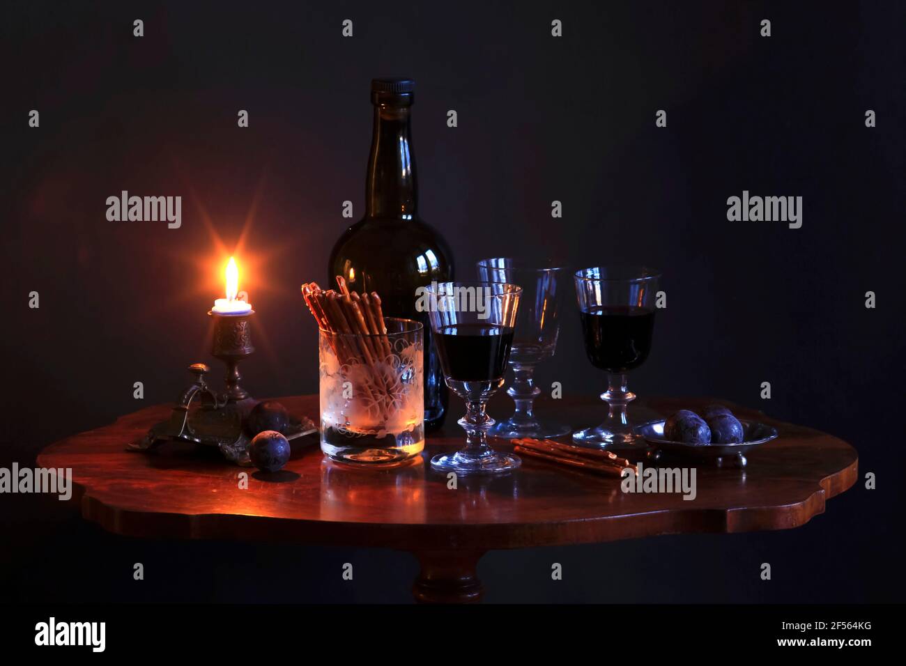Studio photo d'une bouteille de vin rouge, de trois verres de vin, de prunes, de bretzels salés et d'une bougie sur une petite table basse Banque D'Images