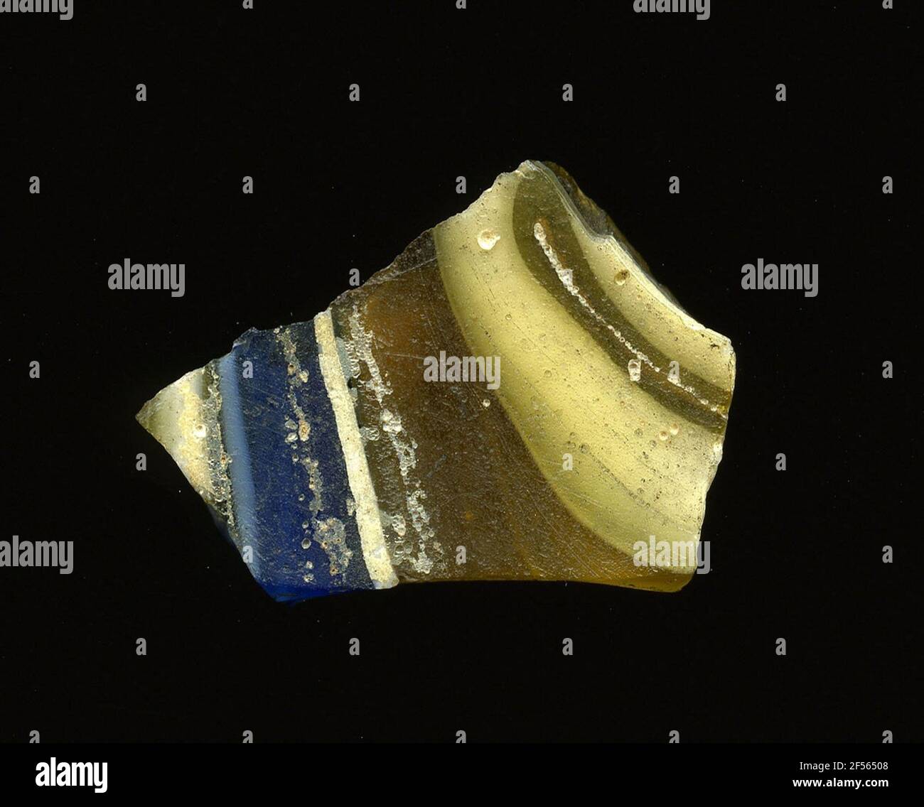 Fragment d'un vaisseau. Une faible courbure du fragment de verre permet l'affectation à un vaisseau, éventuellement à une coque. Le fond blanc de la cisaille est barré de rayures bleues et brunes. En raison du processus de fabrication élaboré et de sa fragilité, le verre a compté aux articles de luxe de l'antiquité. Banque D'Images