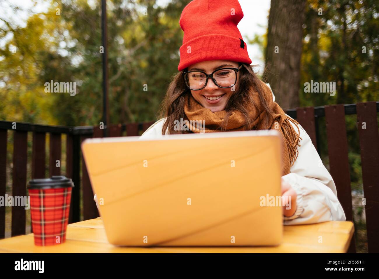 Femme souriante travaillant sur ordinateur portable tout en étant assise au café-terrasse Banque D'Images