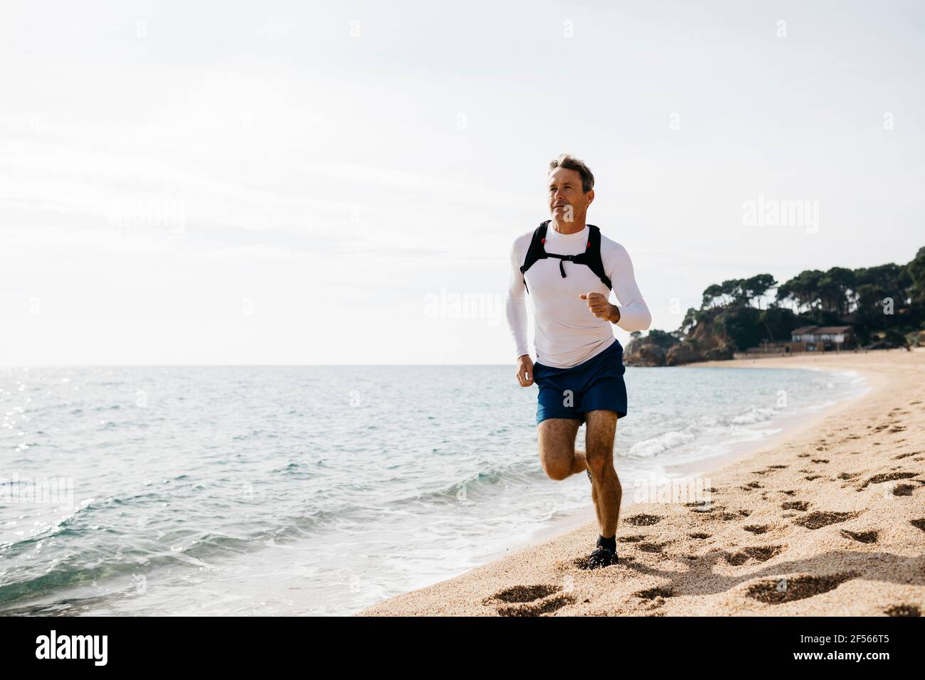 Homme mature qui court sur la plage pendant la journée ensoleillée Banque D'Images