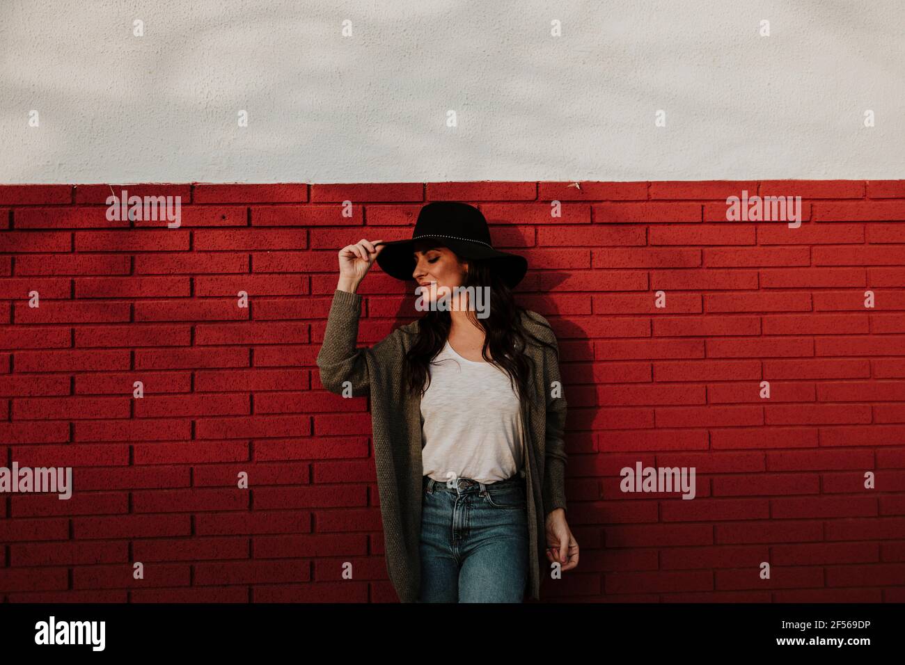 Belle femme en gilet et chapeau pendu sur le mur de briques rouges tout en regardant loin Banque D'Images