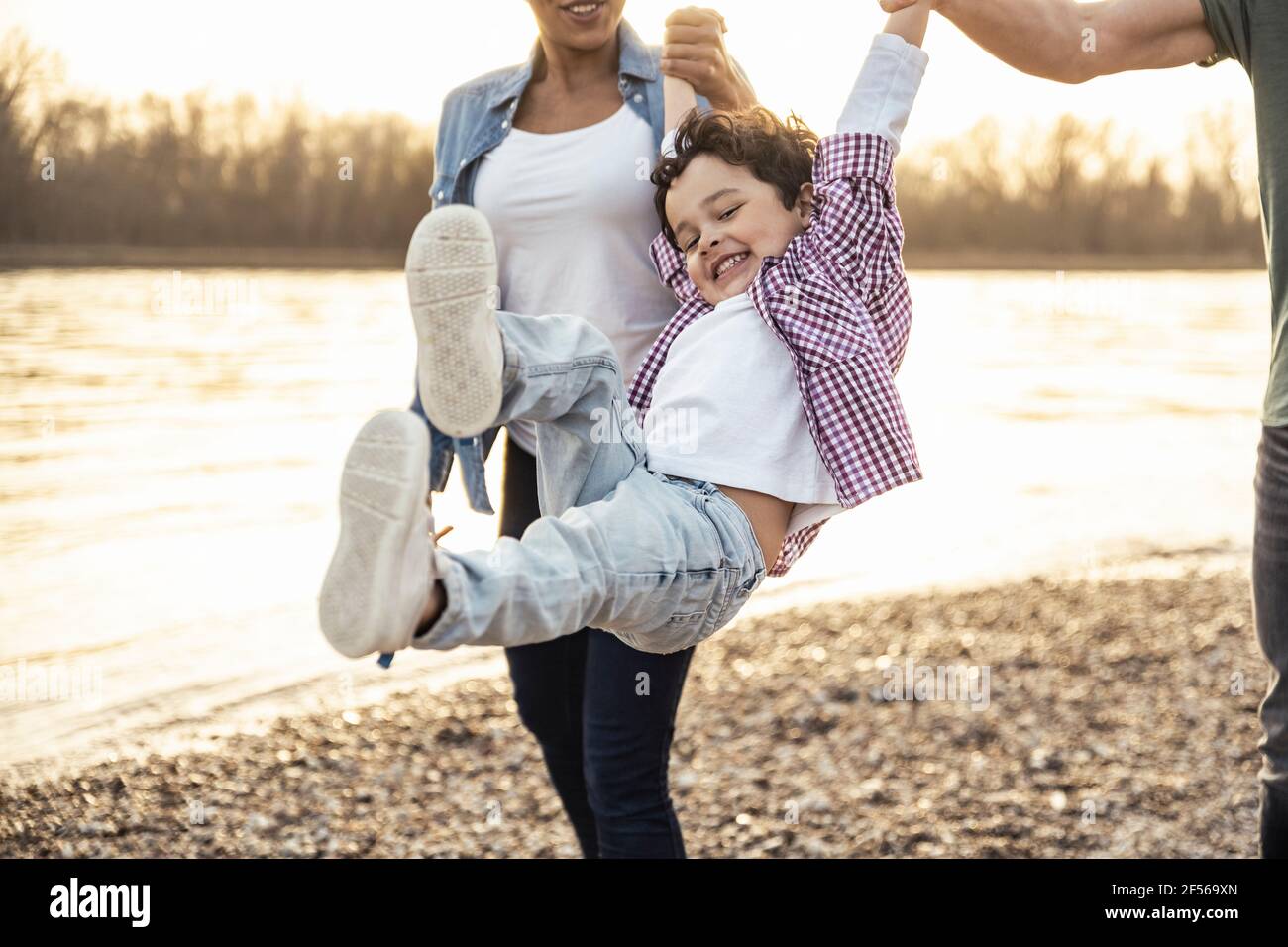 Garçon joyeux tenant les mains des parents tout en balançant au bord du lac Banque D'Images