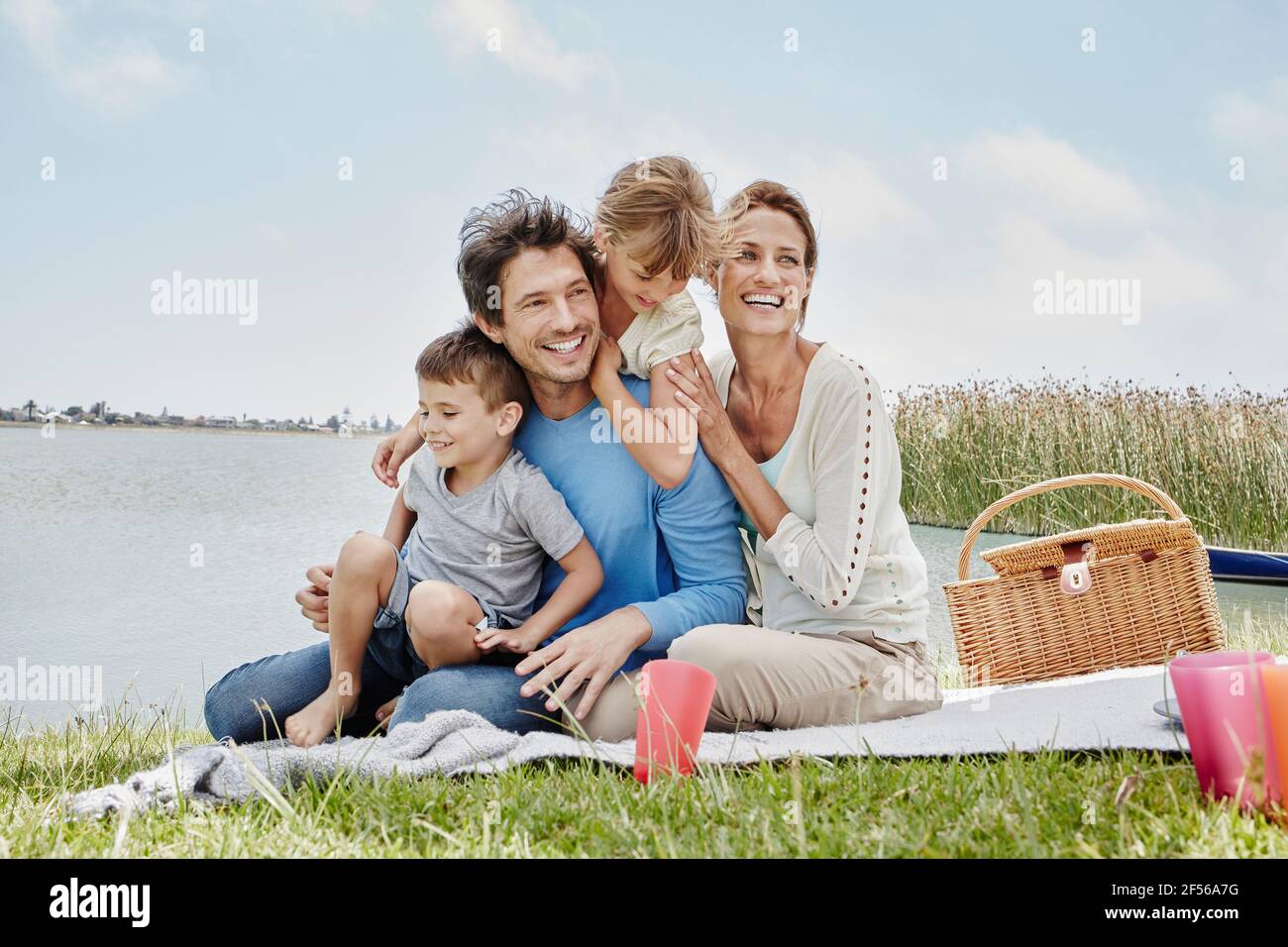 Famille heureuse assise dans une ligne sur une couverture au bord du lac Banque D'Images