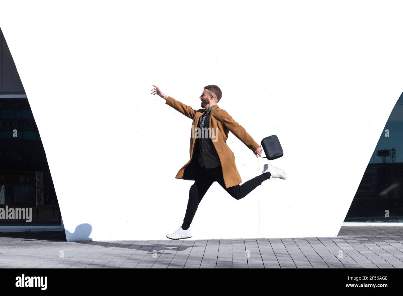 Homme d'affaires avec un petit sac contre un mur blanc Banque D'Images