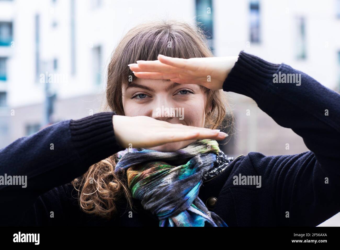 Femme souriante regardant à travers le geste de la main tout en se tenant debout à l'extérieur Banque D'Images