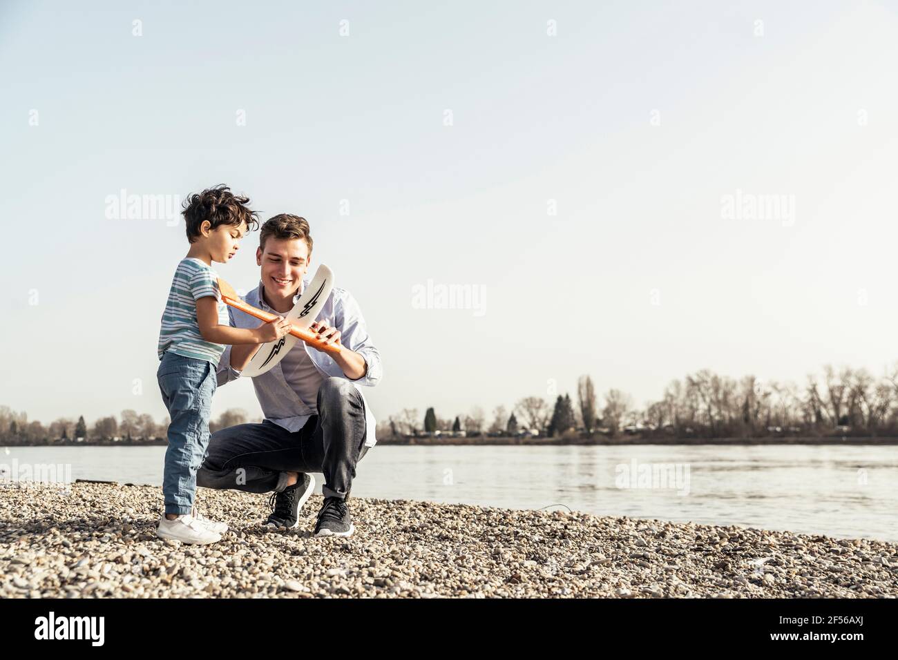 Jeune homme et garçon vérifiant jouet d'avion au bord du lac Banque D'Images
