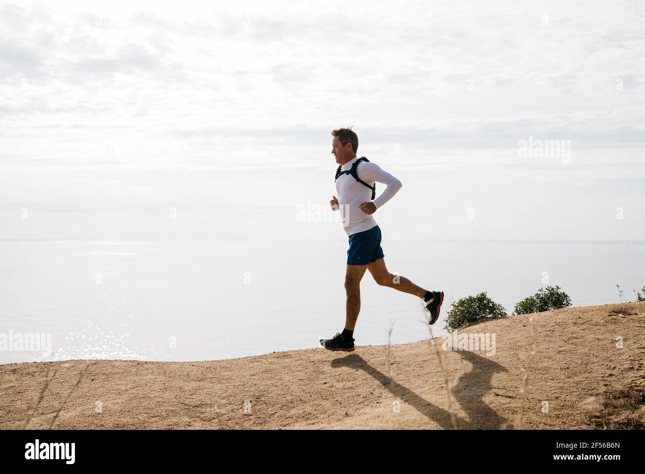 Homme en train de courir sur la route de terre contre le ciel nuageux pendant le soleil jour Banque D'Images
