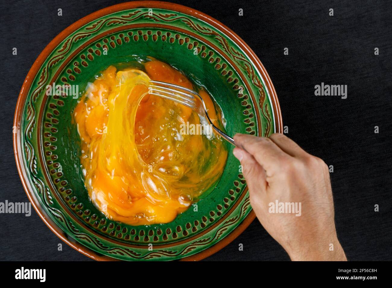 Main de l'homme mélangeant des jaunes d'œufs dans un bol vert Banque D'Images